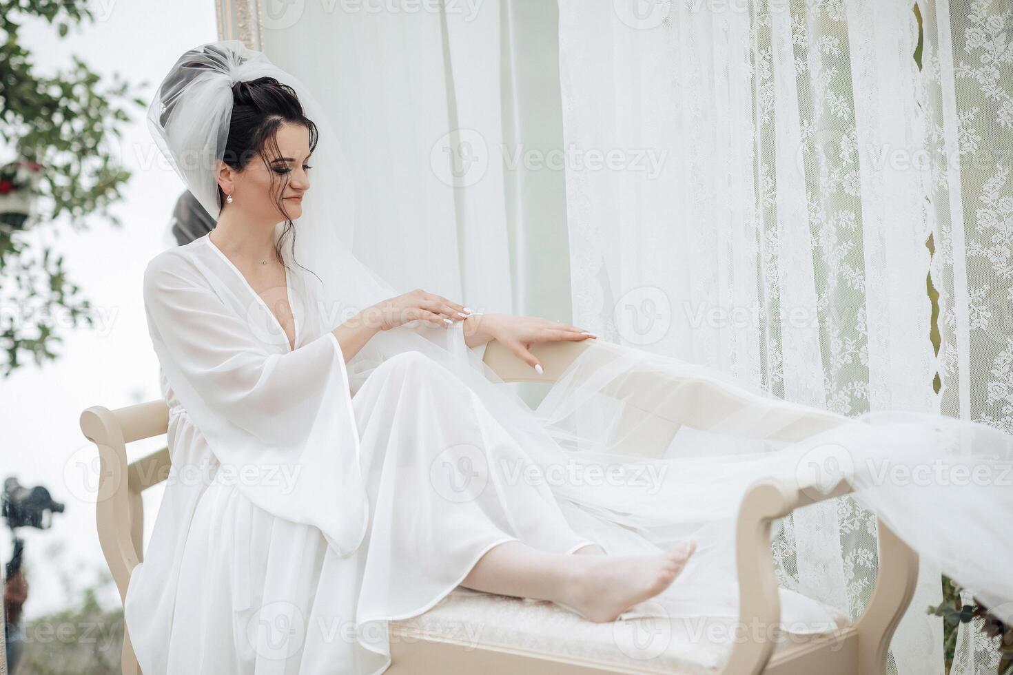 A woman in a white dress is sitting on a chair with a veil on her head. She is wearing a wedding dress and she is getting ready for a wedding photo