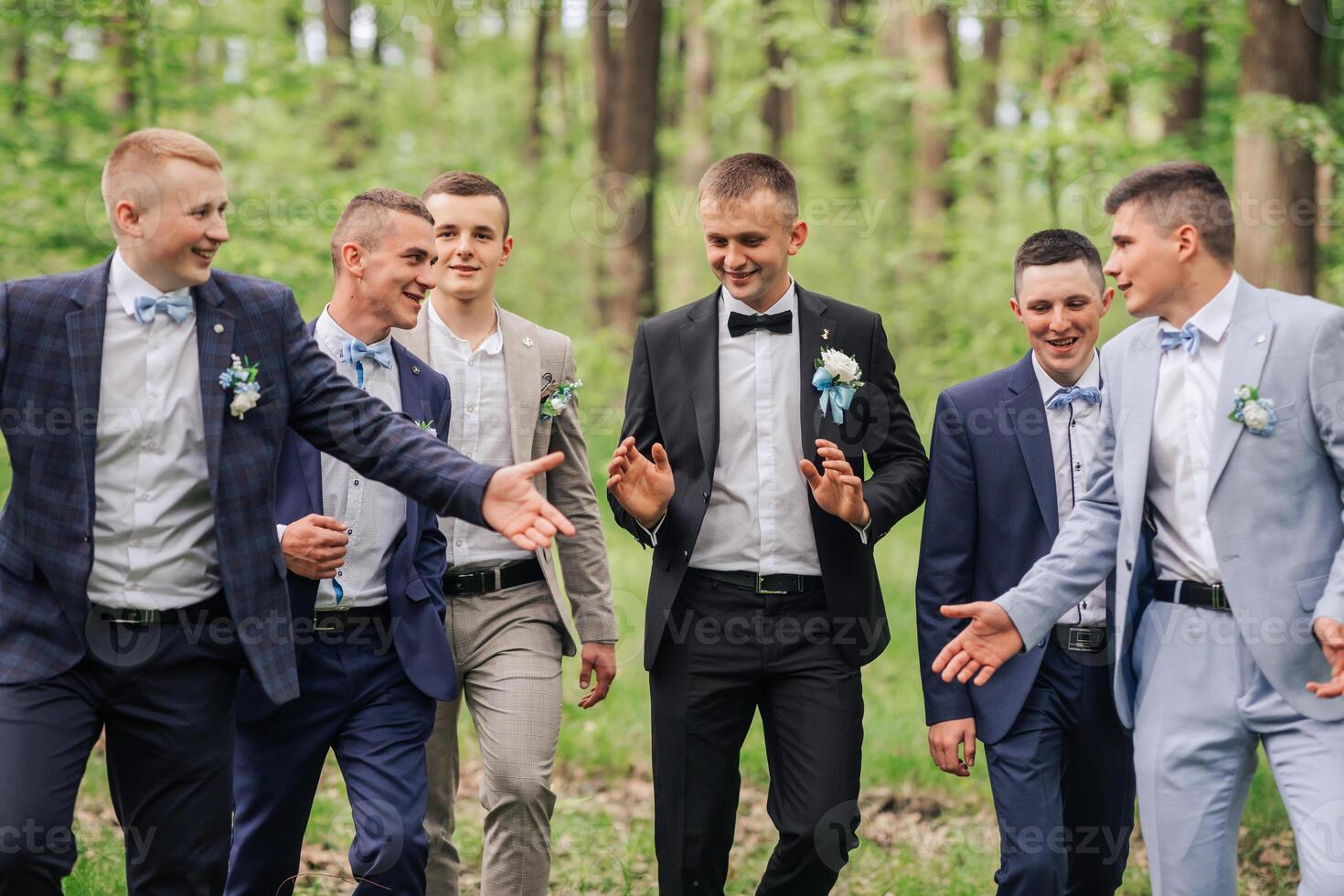 A group of men dressed in suits and ties are posing for a photo in a forest. Scene is lighthearted and fun, as the men are smiling and enjoying each other's company
