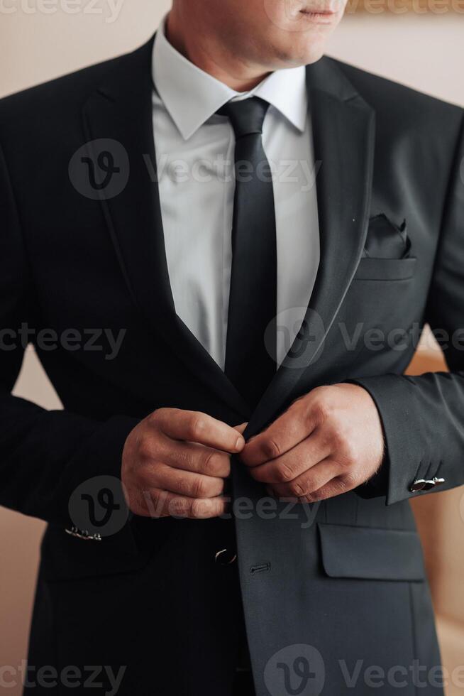 A man in a suit is getting ready to go out. He is wearing a black tie and a white shirt photo