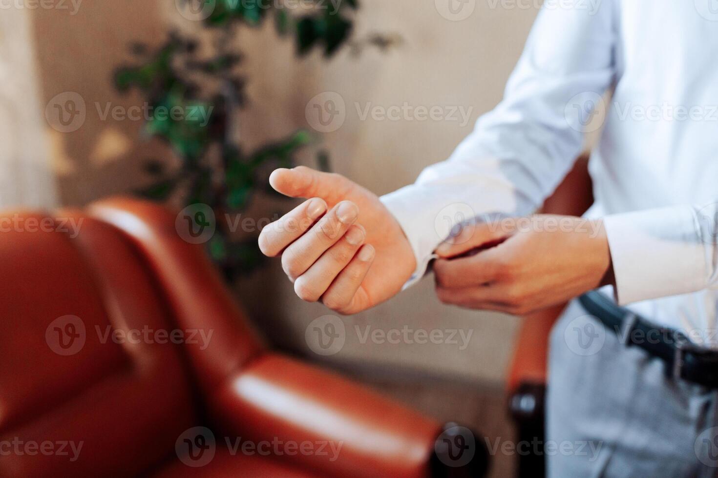 A man is getting dressed in front of a couch. He is wearing a white shirt and gray pants photo