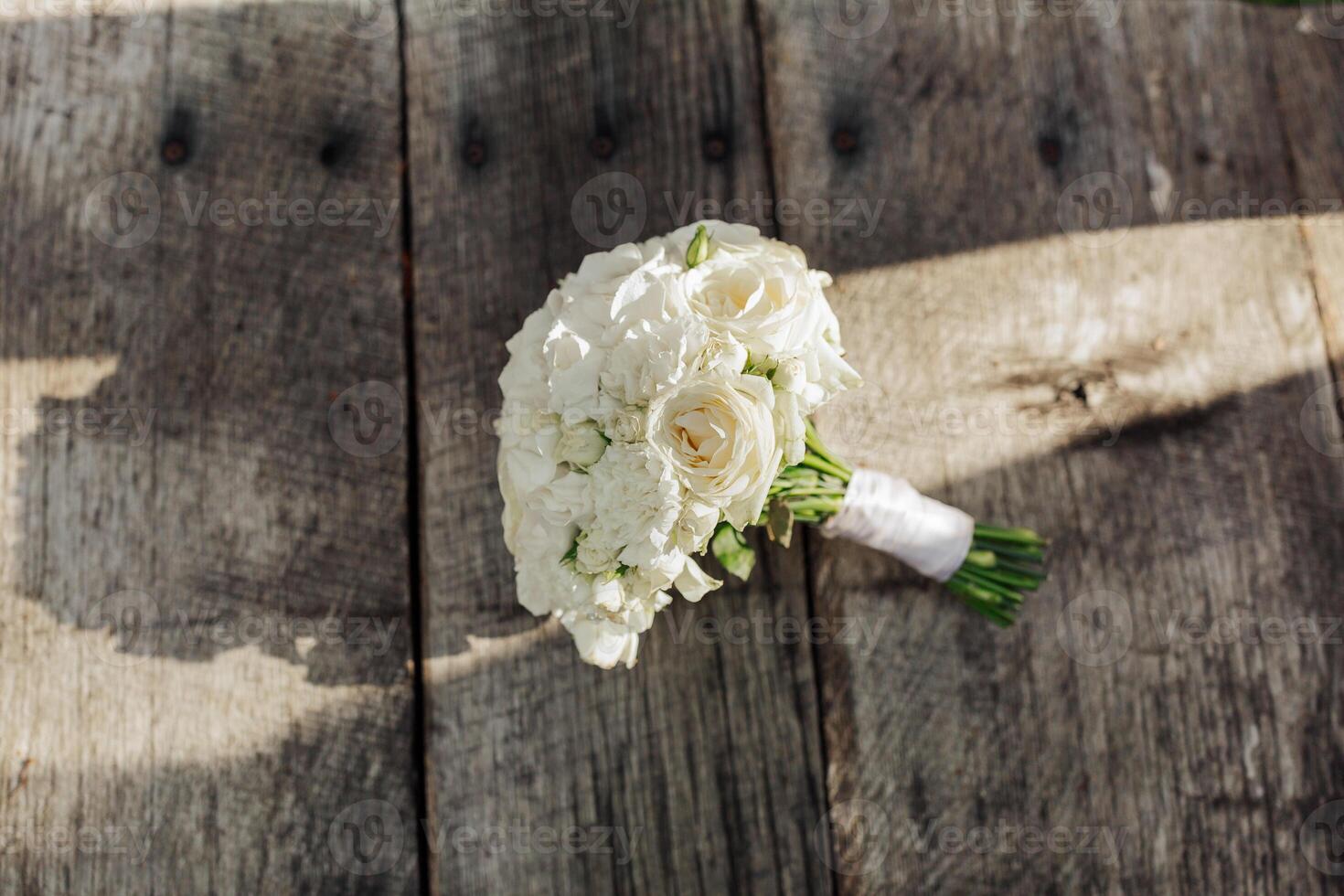 A bouquet of white flowers sits on a wooden table. The flowers are arranged in a vase and are the main focus of the image. The wooden table provides a rustic and natural backdrop for the flowers photo