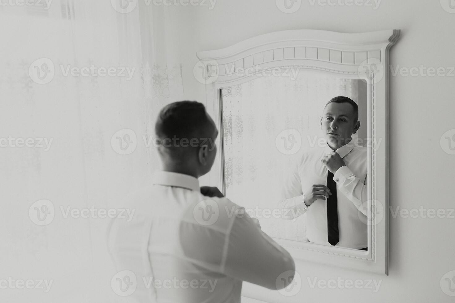 A man is getting ready for a wedding and is adjusting his tie in front of a mirror. Concept of formality and preparation for a special occasion photo