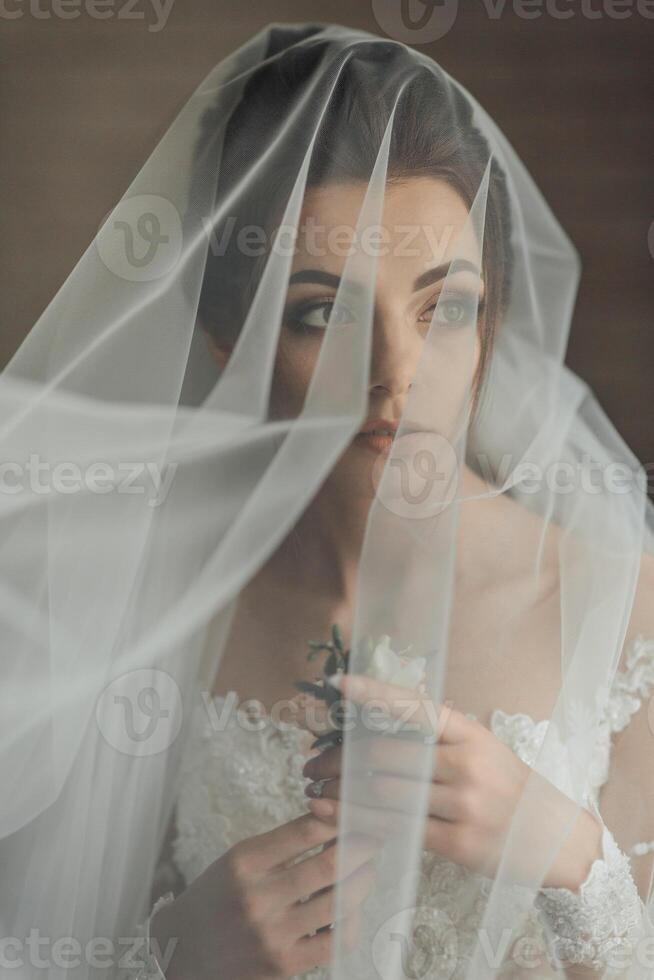 A woman is wearing a veil and holding a flower. The veil is white and covers her face, creating a sense of mystery and elegance photo