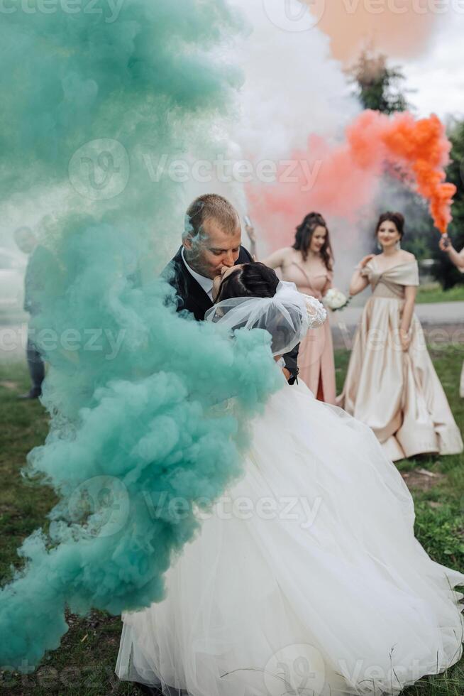 A bride and groom are hugging in the middle of a green and blue smoke. The bride is wearing a white dress and the groom is wearing a black suit. The smoke is coming from a firework photo