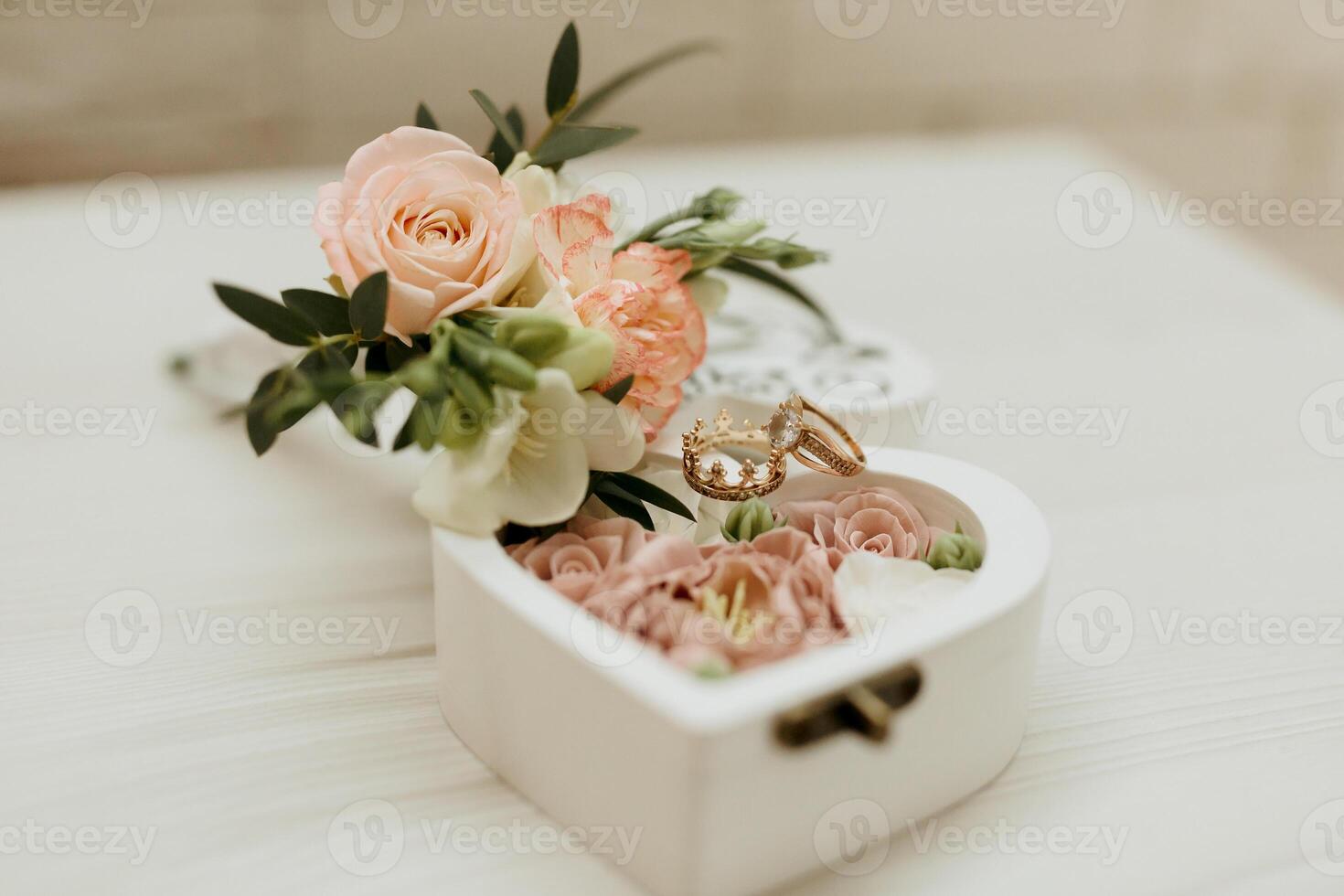 A white box with a heart shape and pink flowers inside. The box contains two rings. The flowers are pink and white, and they are arranged in a way that they look like they are blooming photo