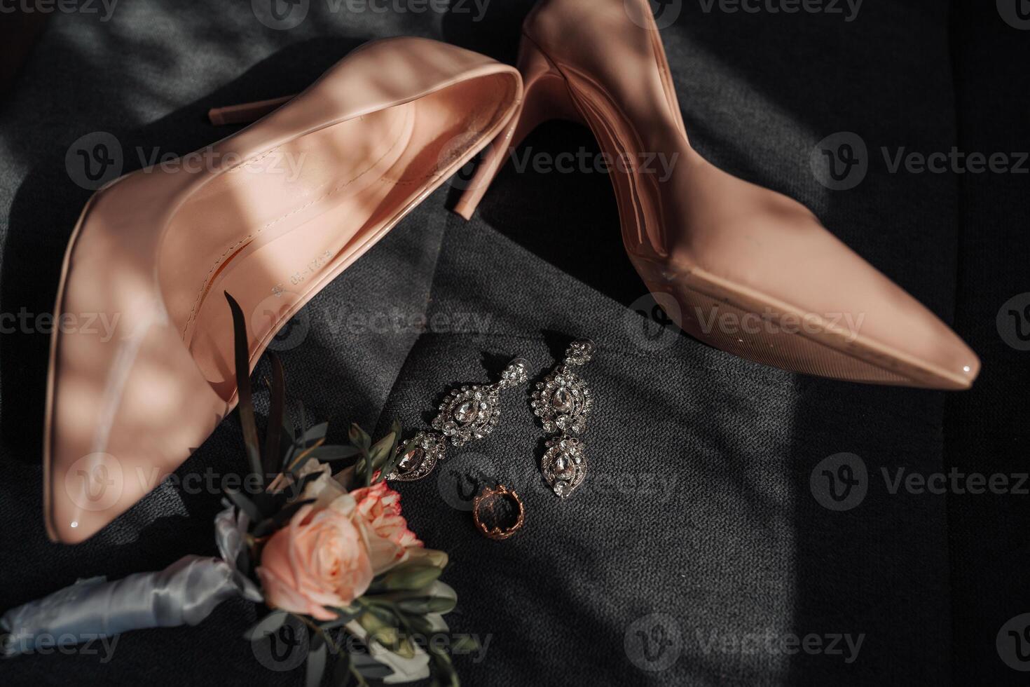 A pair of pink high heels and a pair of earrings are displayed on a table. The earrings are silver and the heels are tall and pointed. Scene is elegant and sophisticated photo