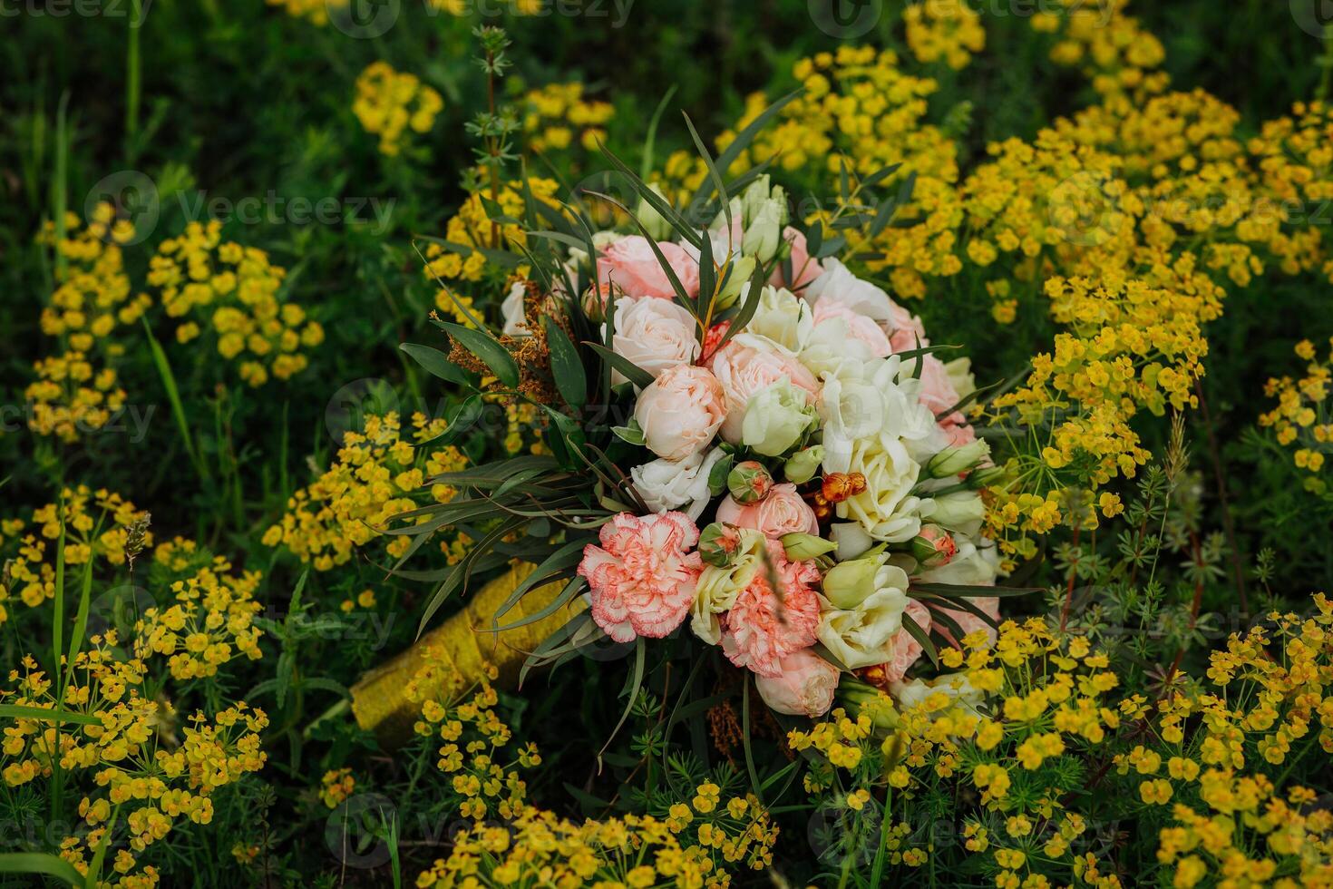 A bouquet of flowers is sitting in a field of yellow flowers. The flowers are pink and white, and the field is lush and green. The scene is peaceful and serene photo