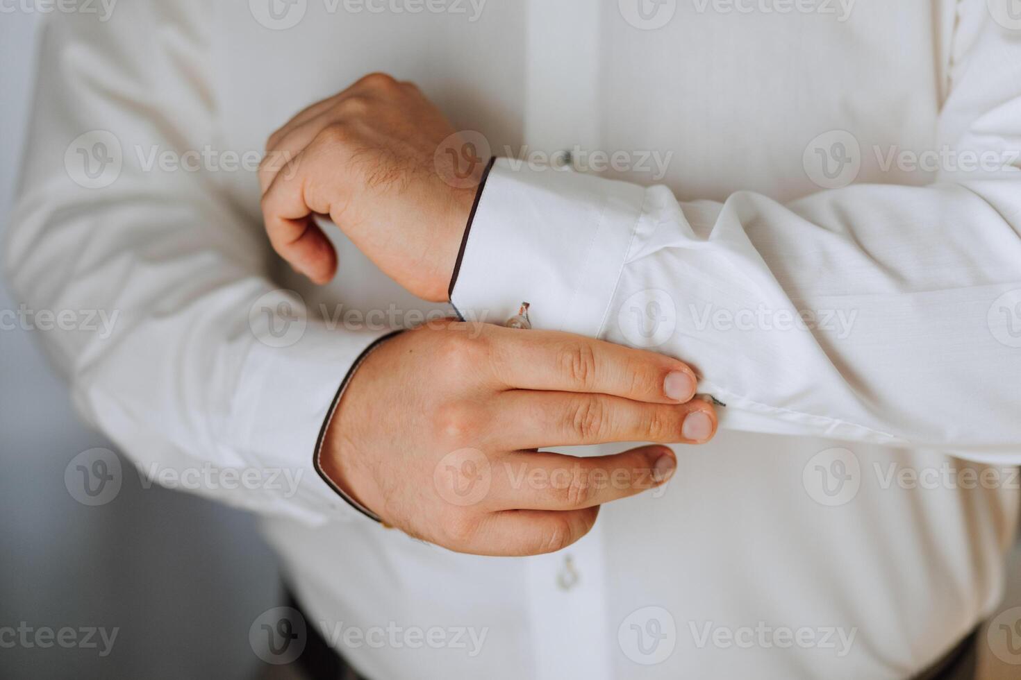 A man is getting dressed in a white shirt and black pants. He is adjusting the collar of his shirt photo