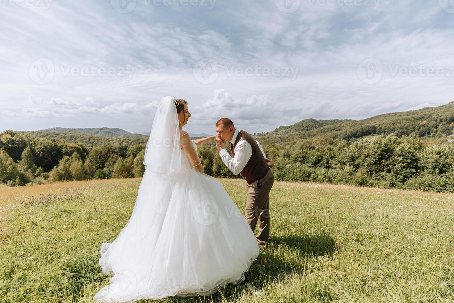 A bride and groom are standing in a field, with the bride wearing a white dress and the groom wearing a vest photo