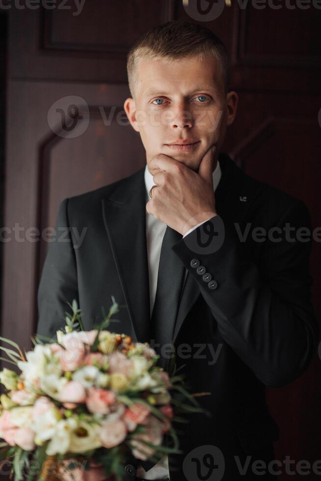 A man in a suit is standing in front of a door with a bouquet of flowers in his hand photo