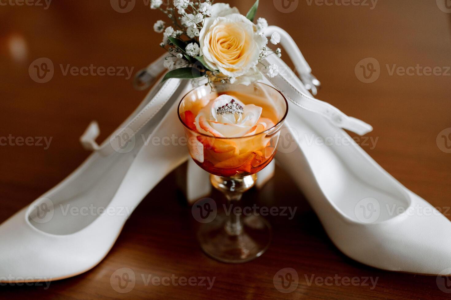A pair of white shoes with a rose on them and a glass of wine. Concept of elegance and sophistication, as the shoes photo