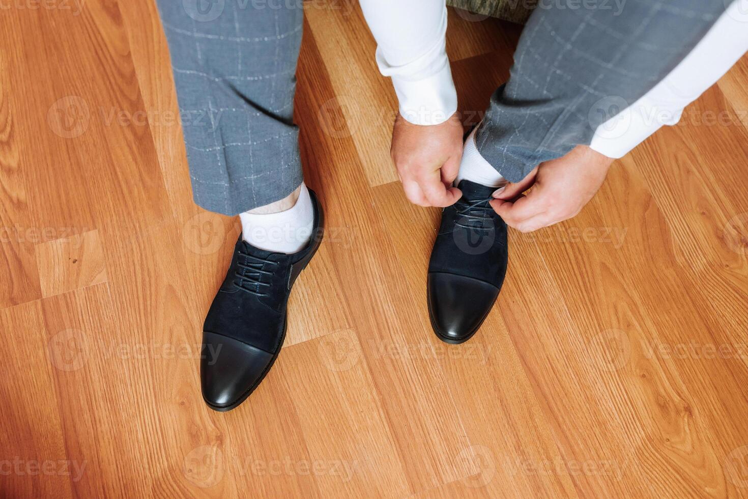 A man is getting ready to put on his shoes. He is wearing a gray suit and white socks photo