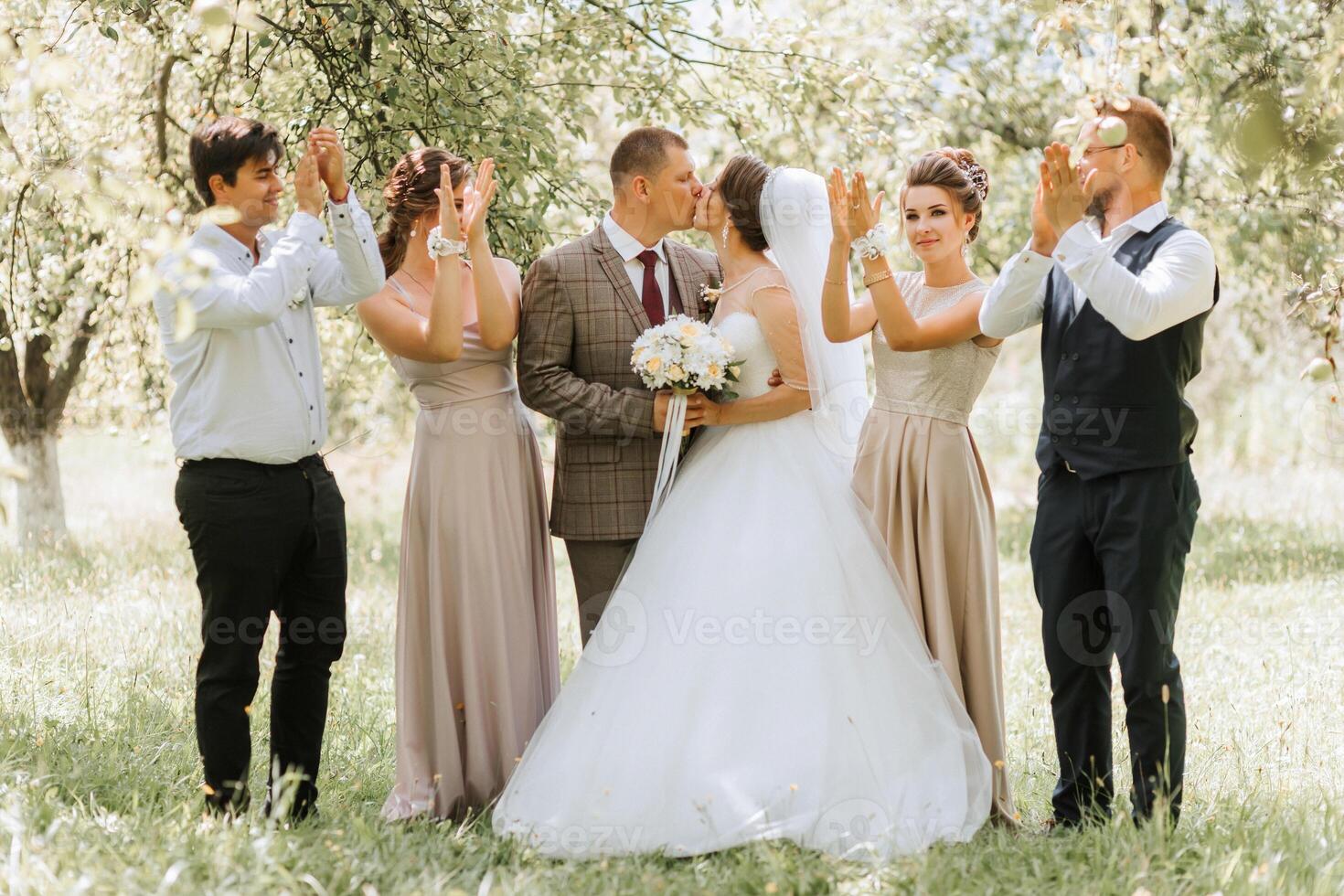 A group of people are posing for a picture, with a bride and groom in the center. The bride is wearing a white dress and the groom is wearing a tie photo