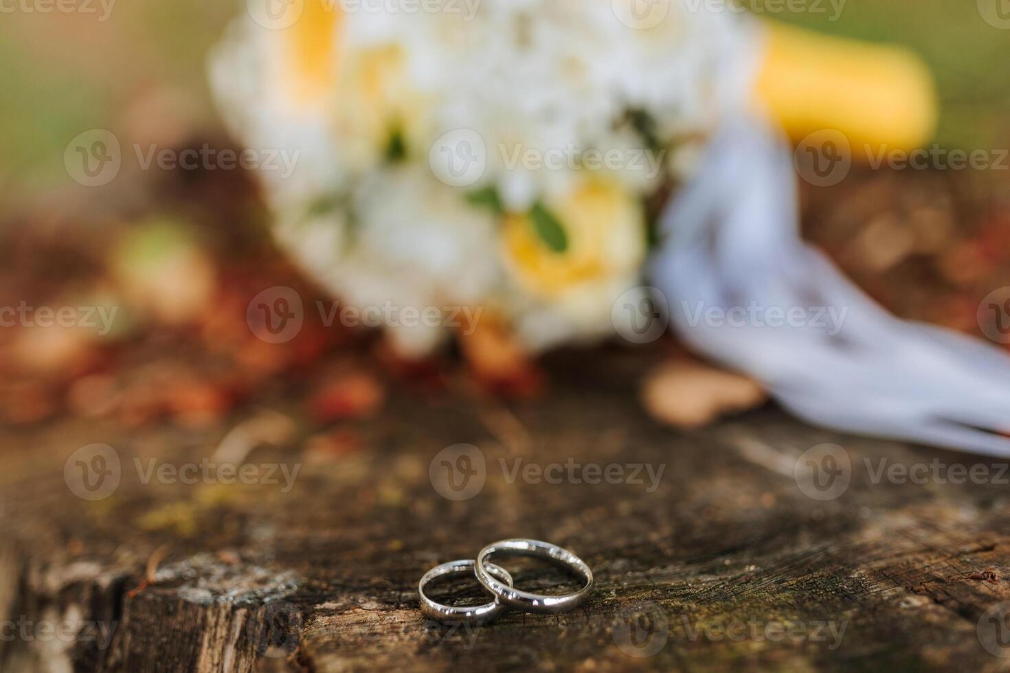 Two wedding rings are on a wooden surface. The rings are silver and are placed next to a bouquet of white flowers. Concept of love and commitment, as the rings symbolize the bond between two people photo