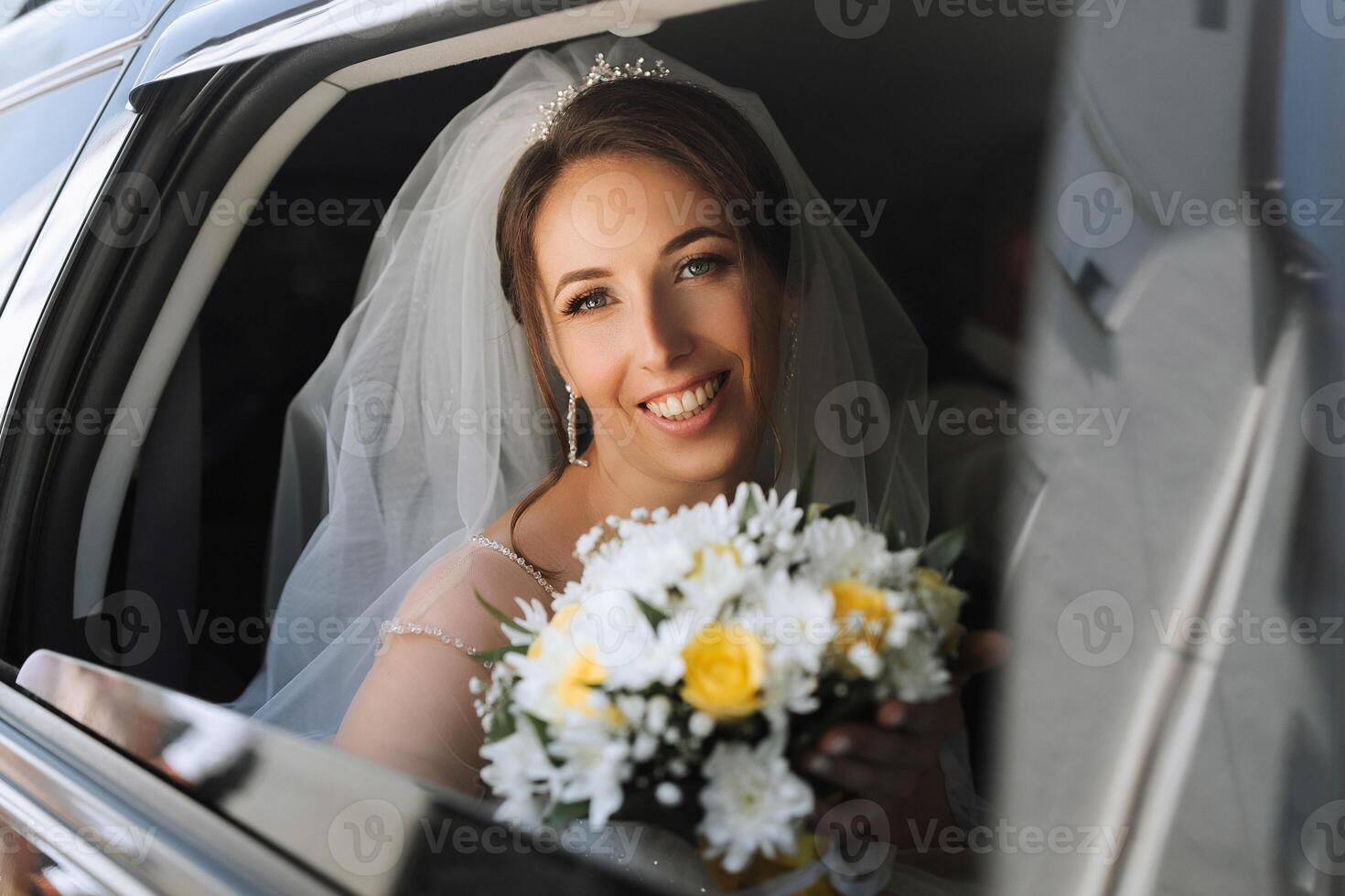 A bride is sitting in a car with a bouquet of flowers. She is smiling and looking out the window photo