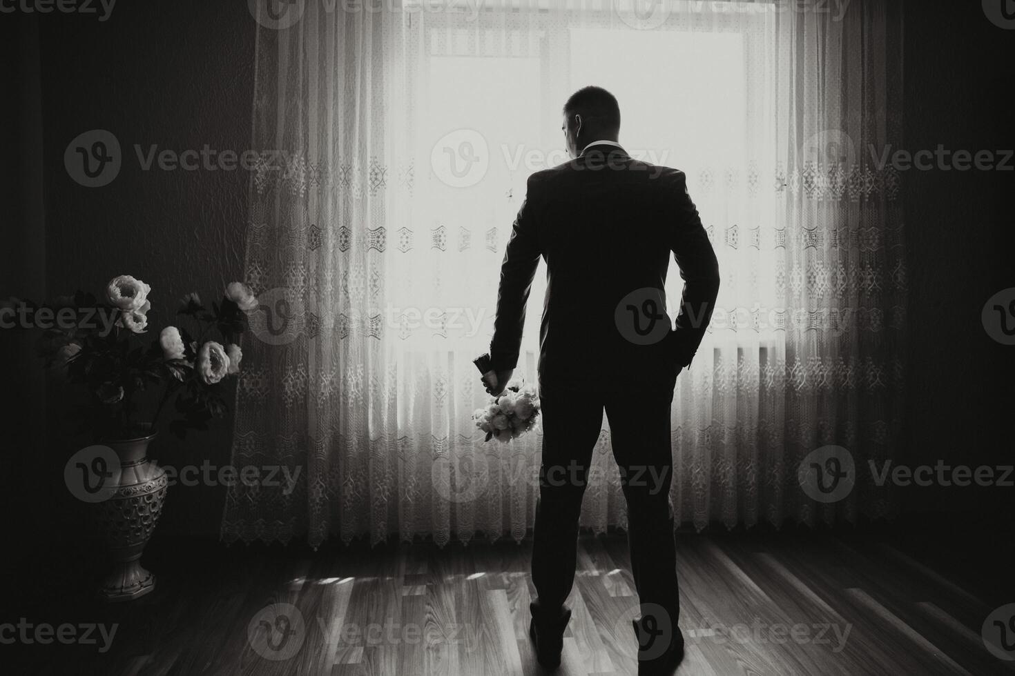 A man in a suit stands in front of a window with a bouquet of flowers in his hand photo