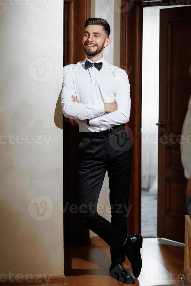 A man in a suit and tie stands in front of a door. He is smiling and he is confident photo