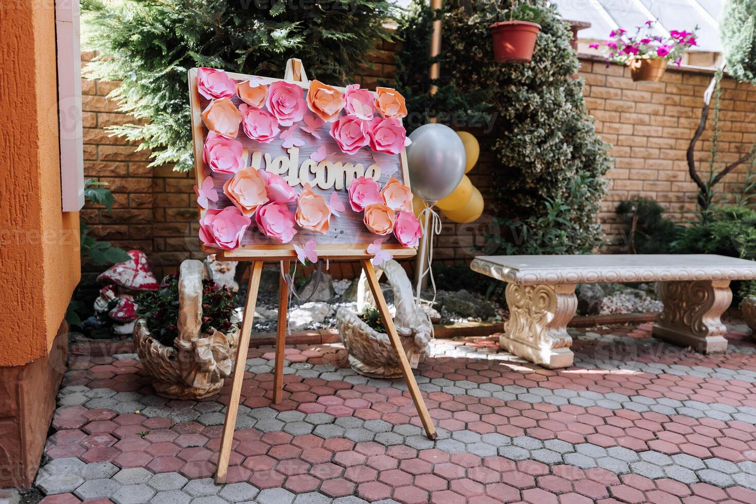 A sign with pink flowers and the word welcome on it is on a wooden stand. A balloon is next to the sign photo