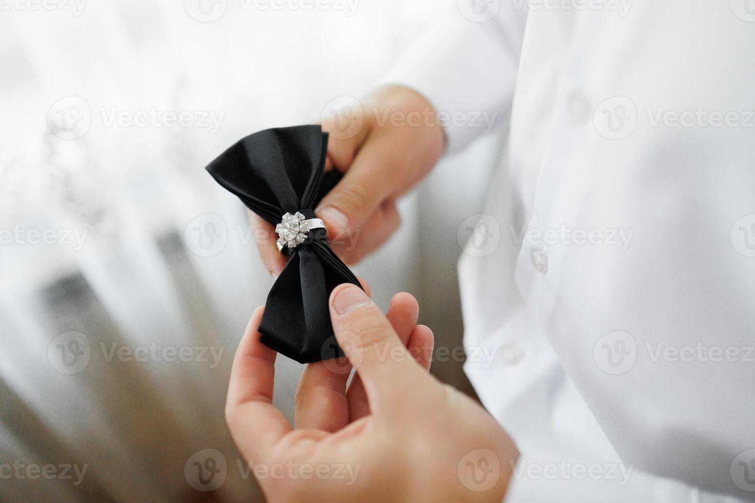 A man is putting on a black bow tie with a diamond ring. Concept of elegance and sophistication, as the man is dressed in a formal outfit. The bow tie and ring add a touch of glamour to the scene photo