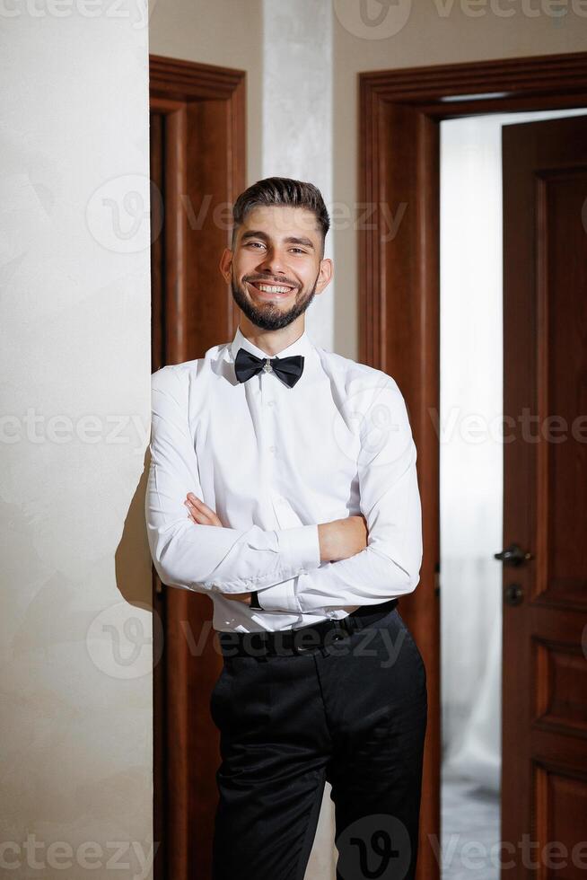 A man in a suit and tie is standing in front of a door. He is smiling and looking at the camera photo