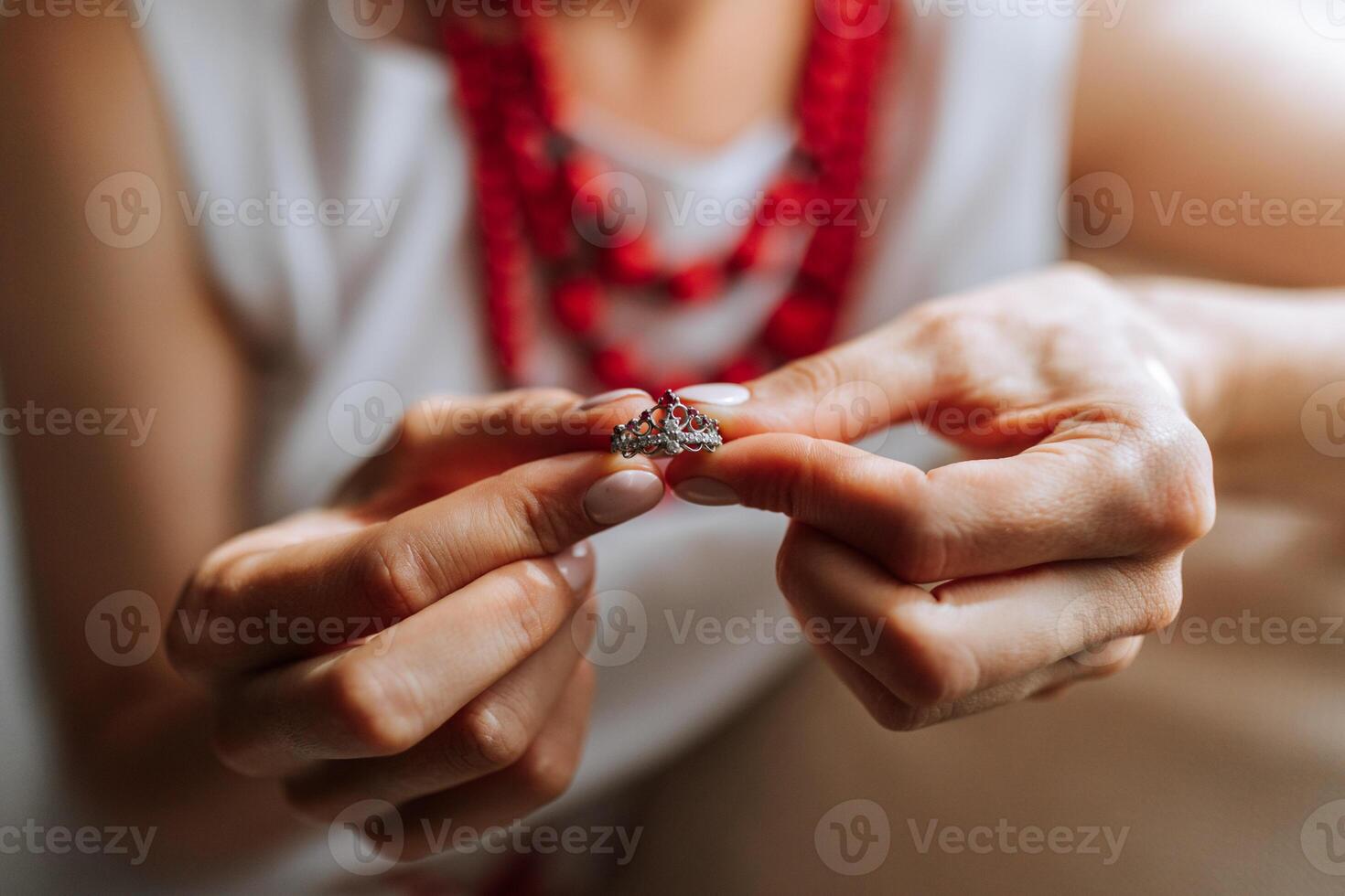 A woman is holding a ring in her hand. The ring is a diamond ring with a red band. The woman is wearing a white shirt and a red necklace. Concept of elegance and sophistication photo