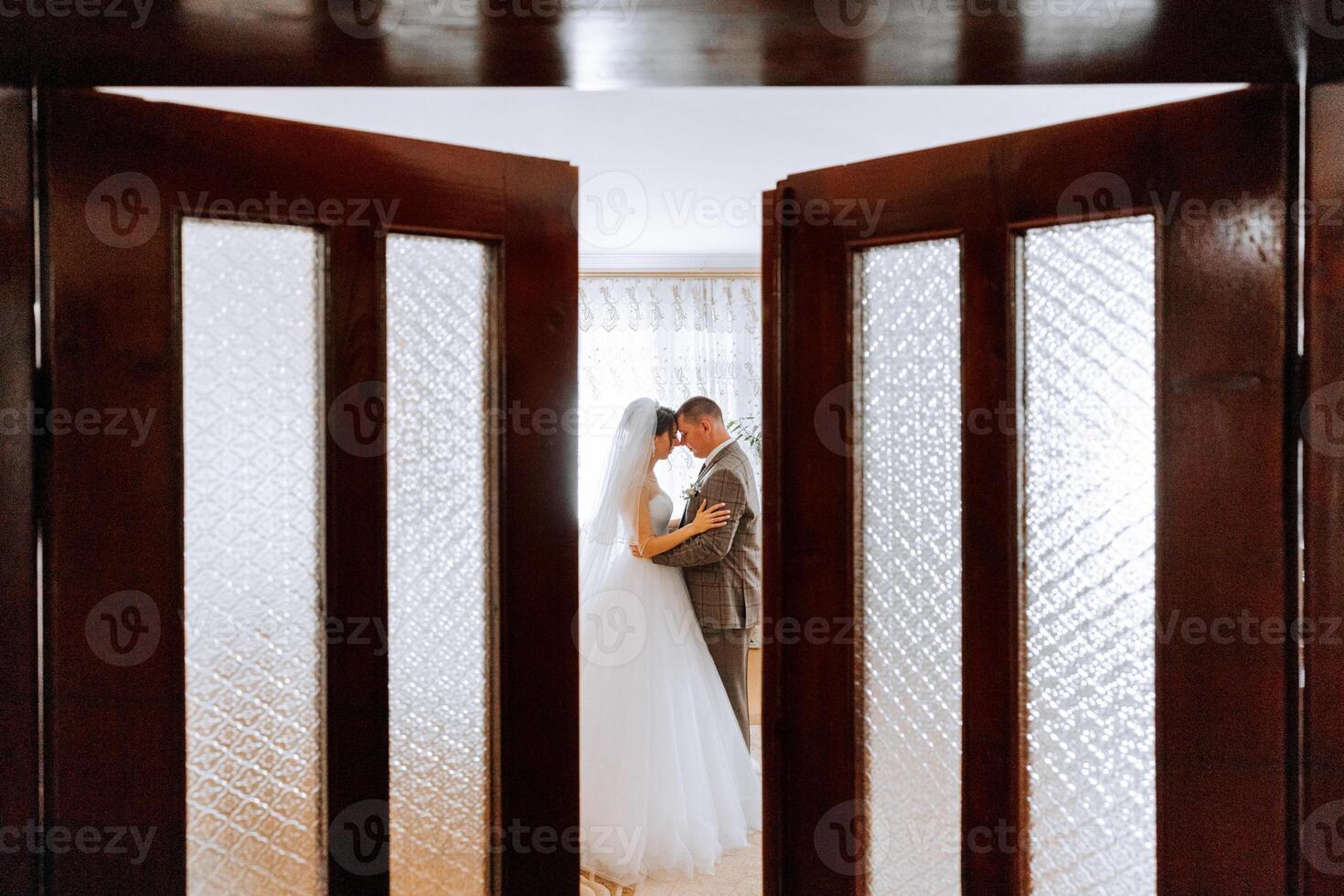 A bride and groom are kissing in front of a door. Scene is romantic and intimate photo