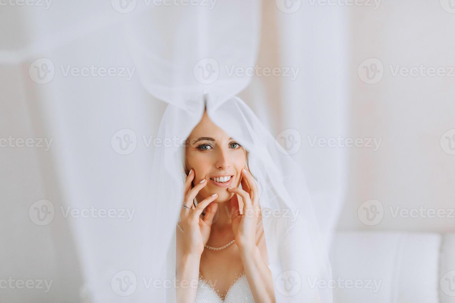A bride is posing for a picture with her veil covering her face. She is wearing a white dress and has her hands on her face. Concept of intimacy and closeness between the bride and the photographer photo