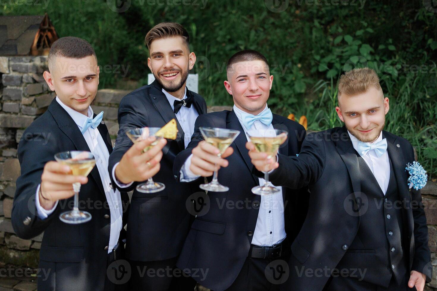 A group of men in suits are holding up glasses of champagne and smiling. Scene is celebratory and happy photo