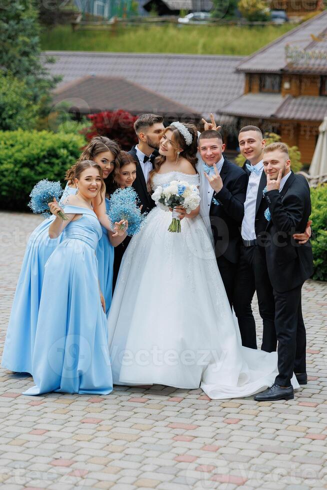 A bride and groom are posing for a picture with their wedding party. The bride is wearing a white dress and the groom is wearing a suit photo