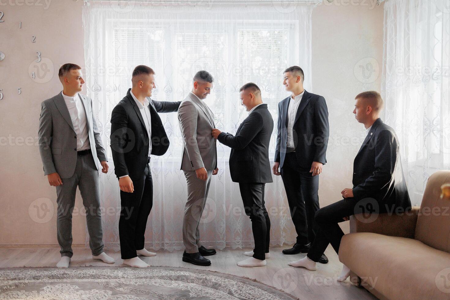 A group of men are dressed in suits and ties, with one man helping another adjust his tie. Scene is formal and professional, as the men are getting ready for a special occasion or event photo