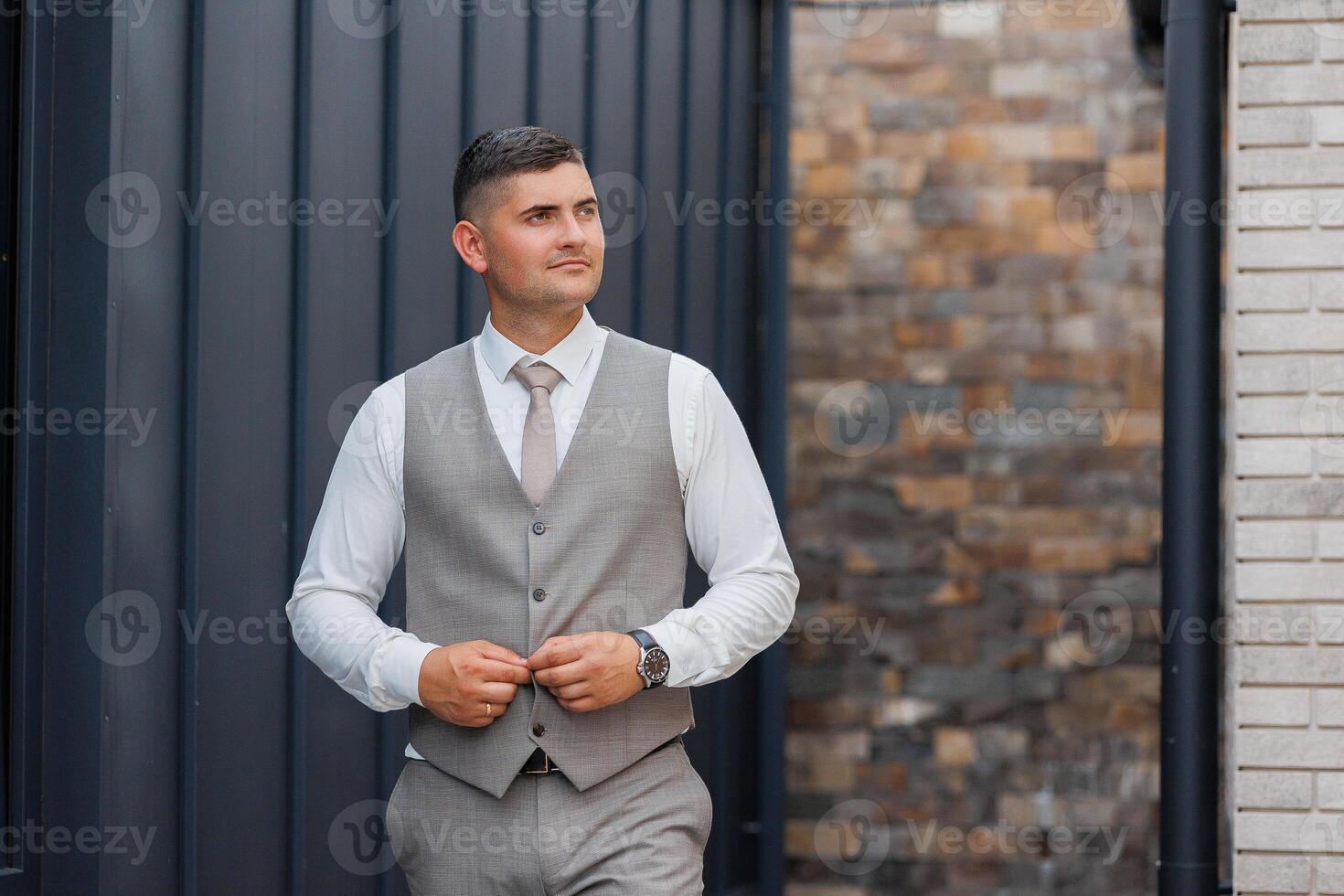 A man in a suit and vest stands in front of a brick wall. He is wearing a tie and he is getting ready for an event photo