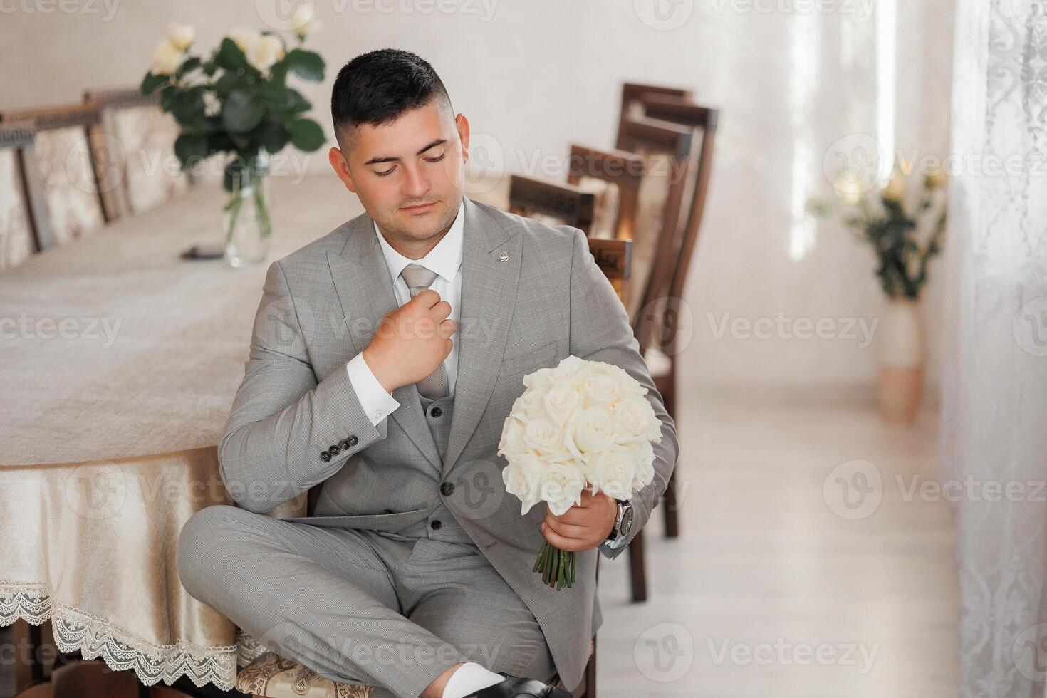 A man in a suit is sitting at a table with a bouquet of white flowers in his lap photo