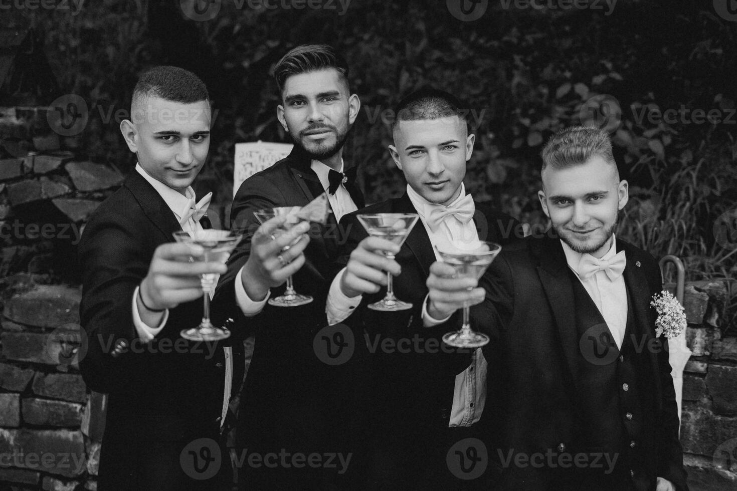 Four men in suits are holding glasses of wine and smiling. Scene is celebratory and happy photo