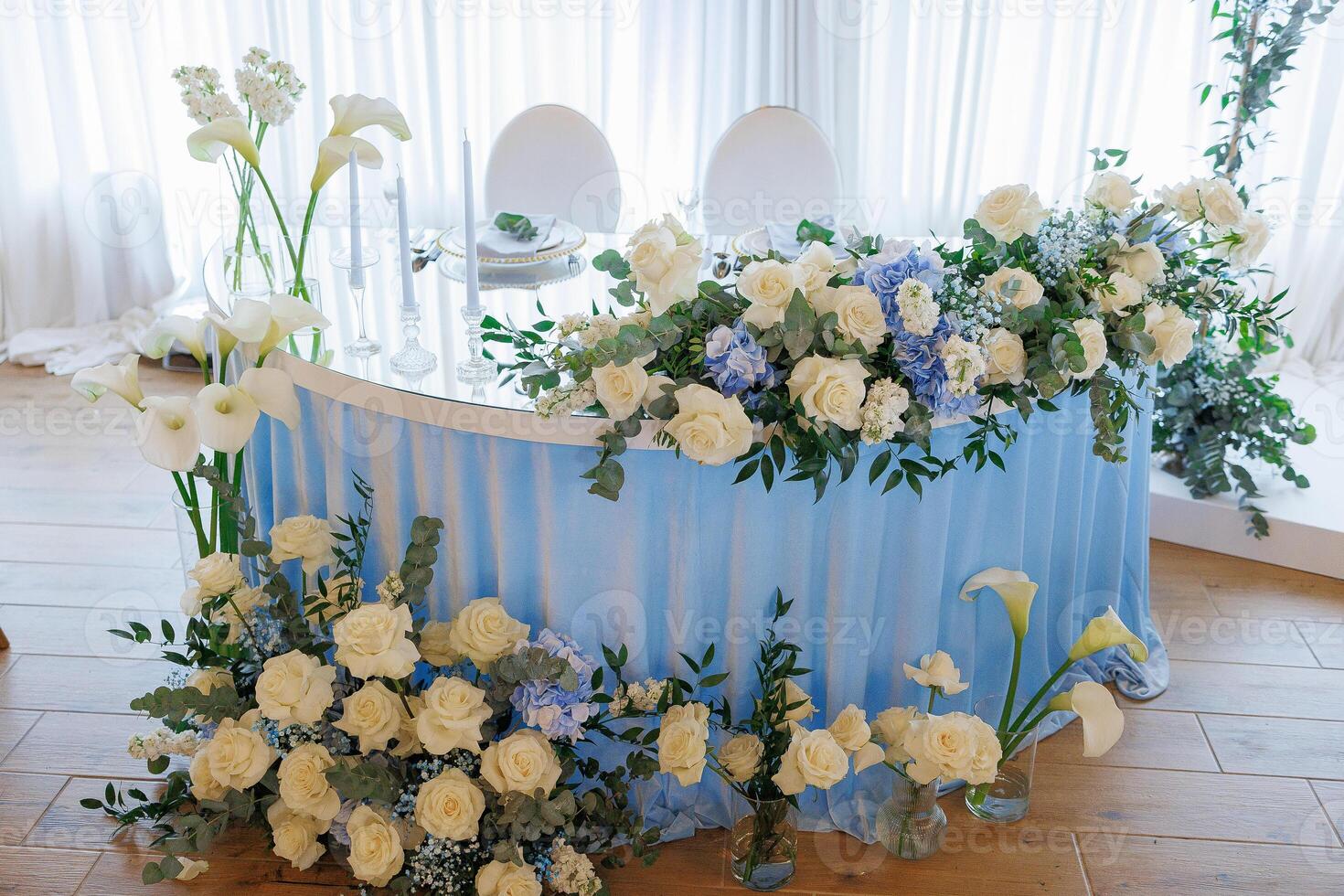 A blue table with white flowers and candles on it. The table is decorated with flowers and candles, and there are two chairs on either side. The table is set for a special occasion, and the flowers photo