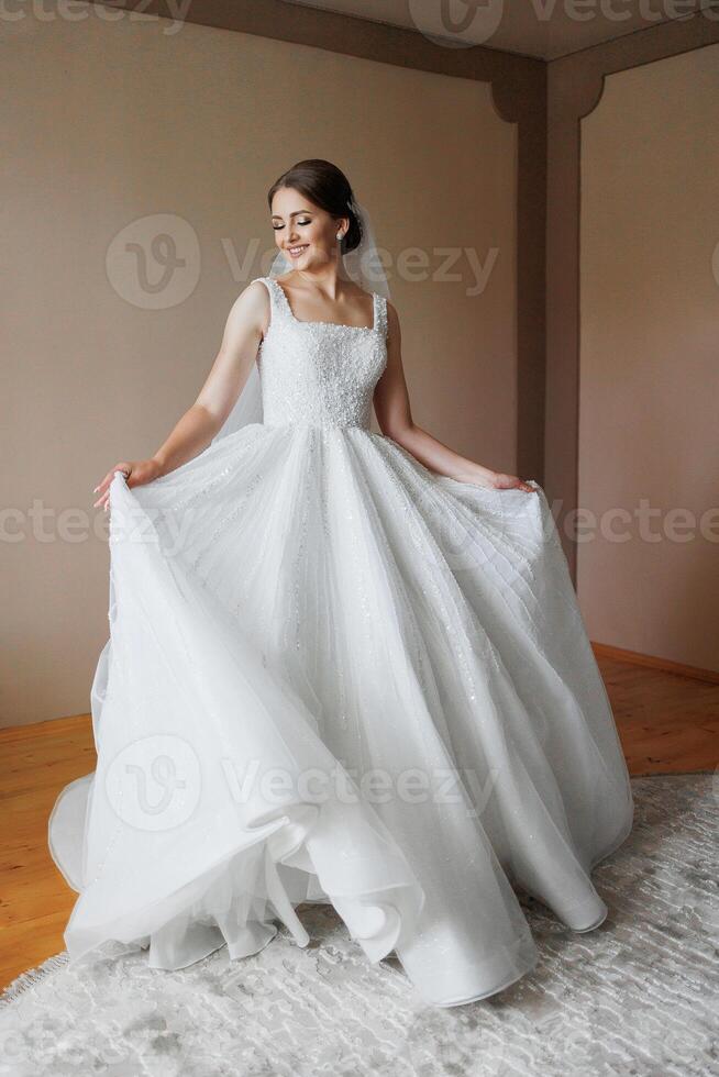 A bride in a white dress is posing for a picture. She is wearing a veil and has her arms outstretched. The image has a happy and celebratory mood, as it captures a special moment in the bride's life photo