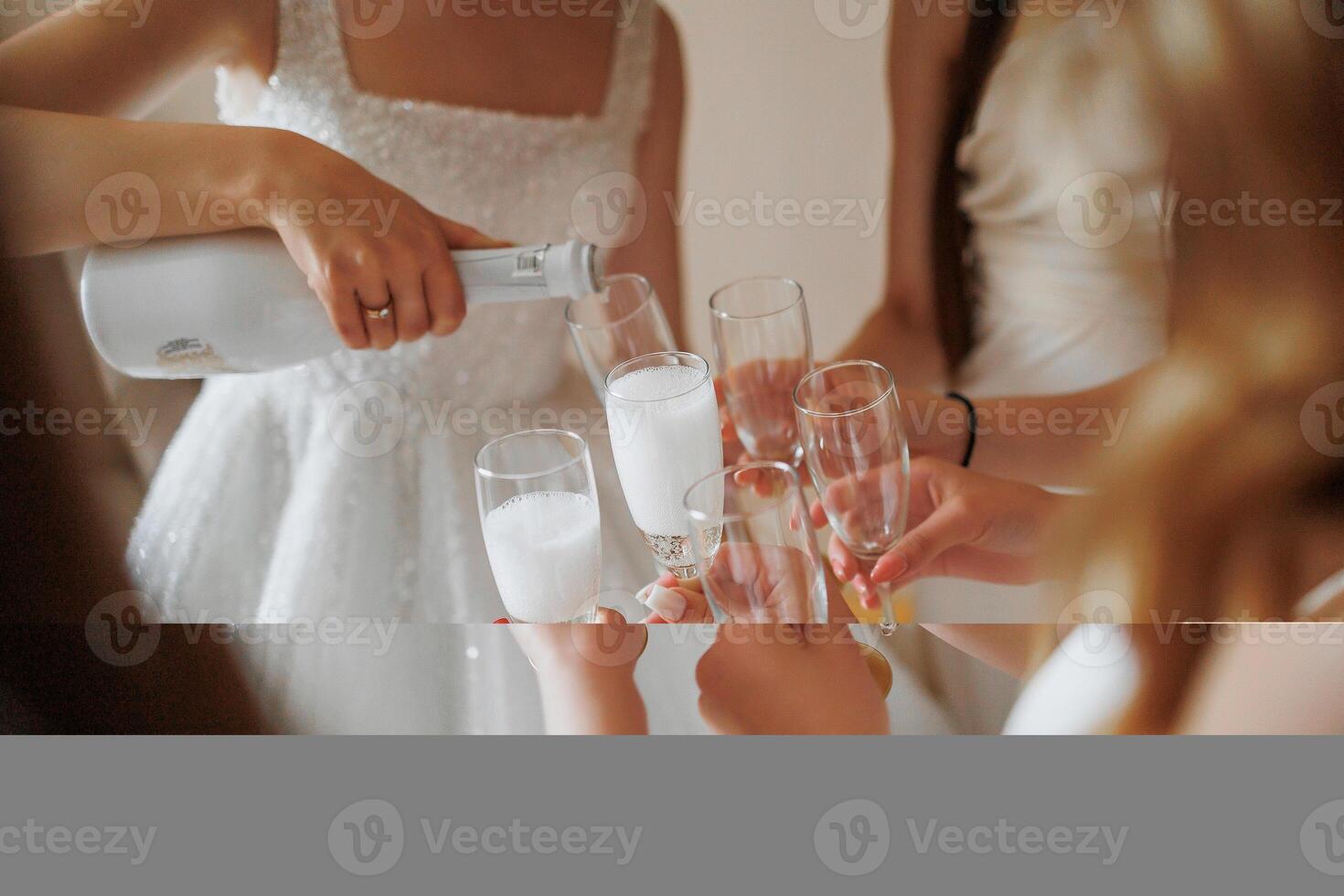 A group of women are celebrating a special occasion by toasting with champagne. One woman is pouring the champagne into the glasses while the others hold their glasses up to their lips photo