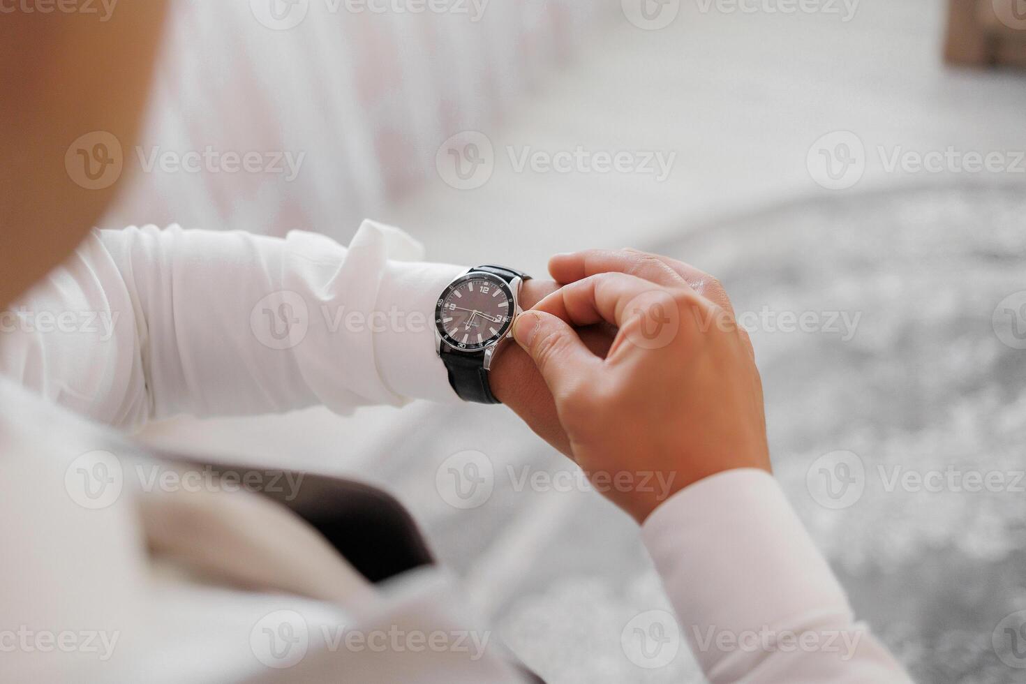 A man is wearing a watch and looking at it. The watch is black and has a silver band photo