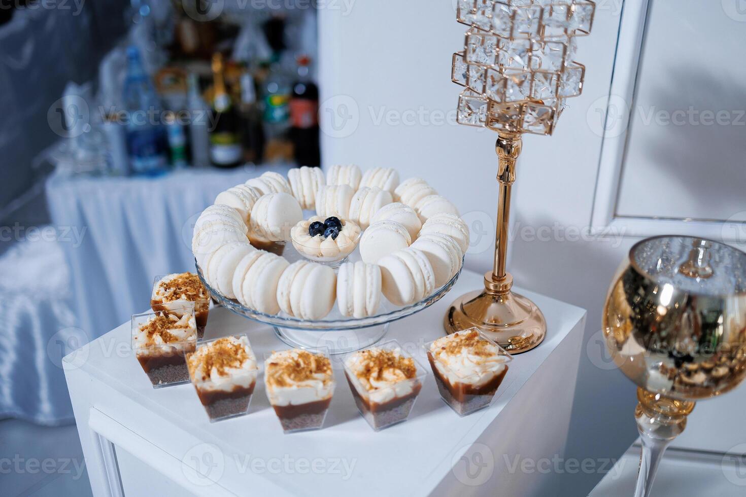 A table with a variety of desserts, including macaroons and cakes, and a tall glass vase with a candle in it photo