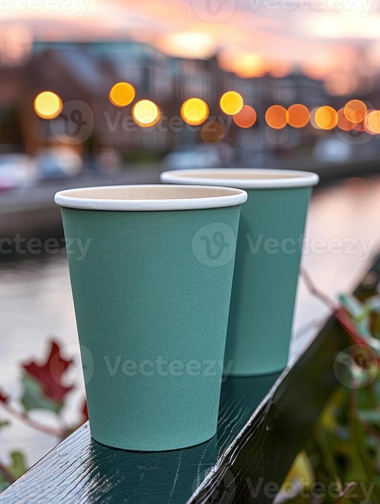 Two teal paper cups on a railing with city lights in the background photo