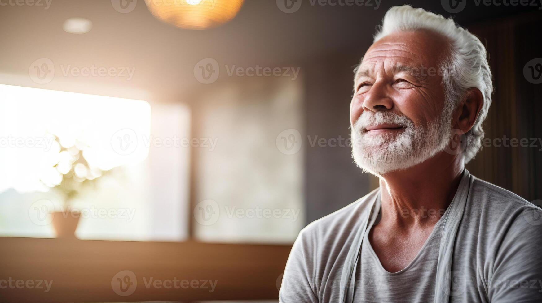 Serene senior man with white hair and beard smiles while looking up at the sunlight streaming through a window. His peaceful expression reflects contentment and hope. photo