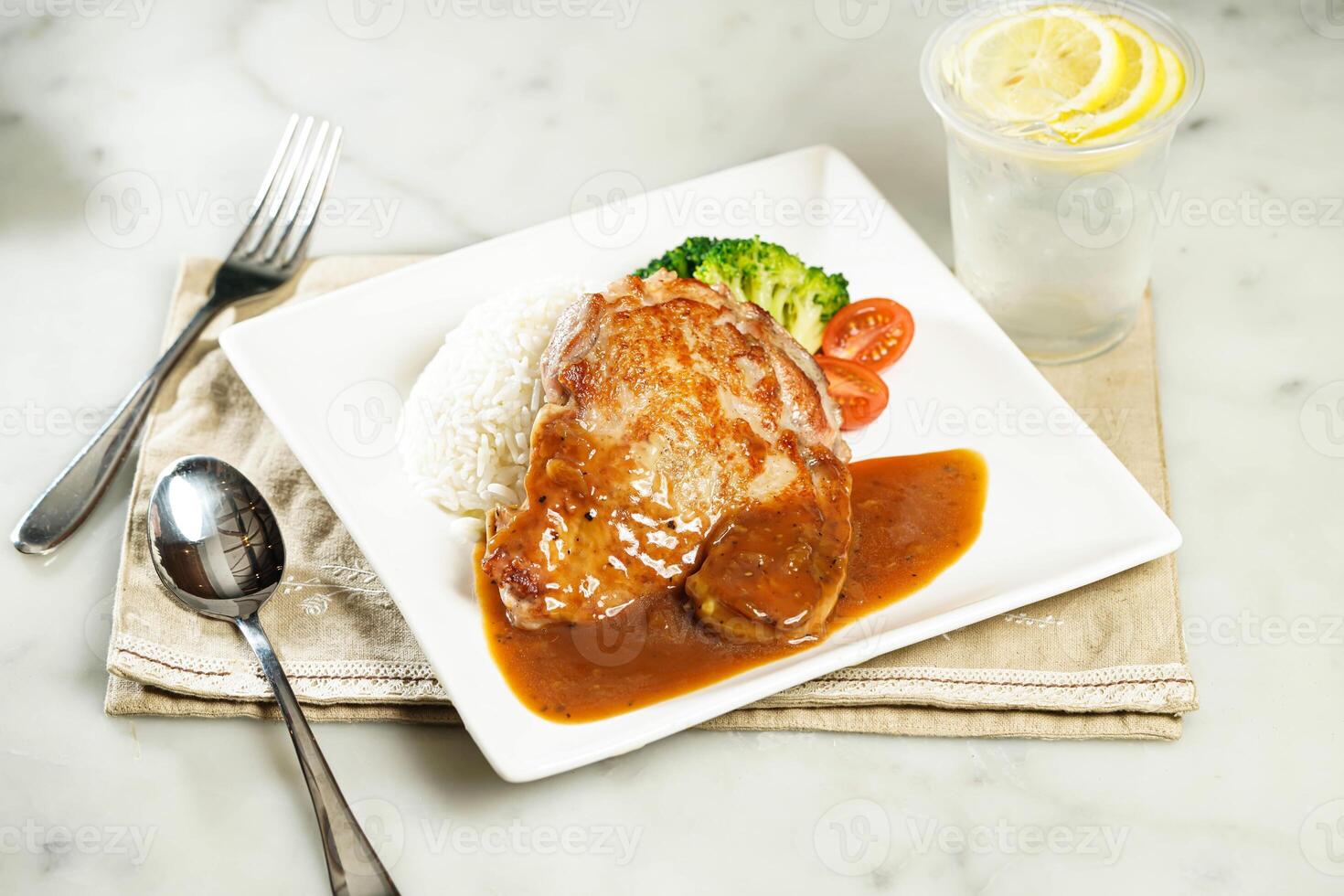 Crispy Chicken Steak with Rice in Black Pepper Sauce with lemonade, fork and spoon, served in dish isolated on napkin side view of asian food photo
