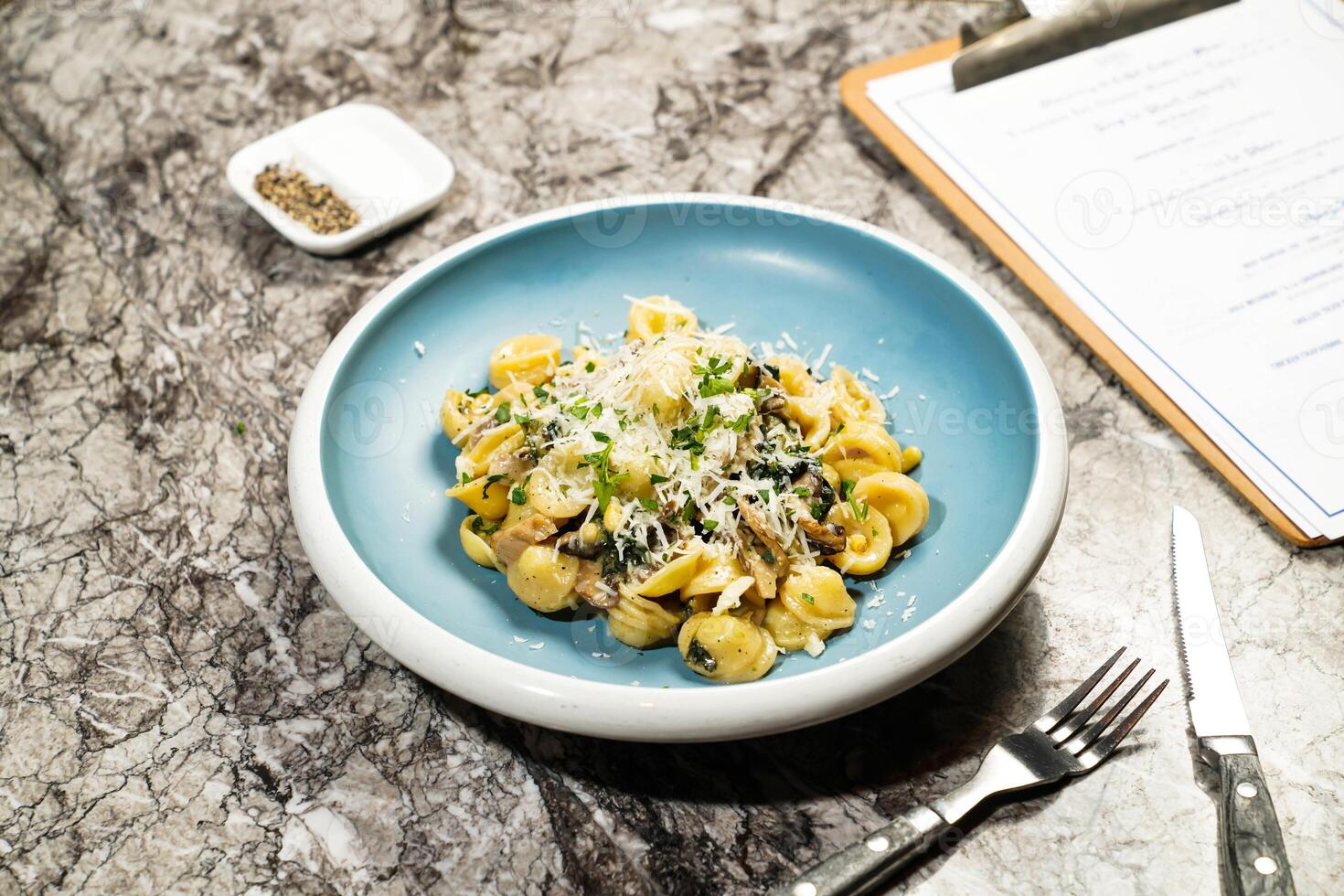 Orecchiette Pasta with Spinach, Mushrooms and Pine Nut, Cooked with White Wine and Pecorino Romano Cheese, fork and knife served in plate isolated on marble background side view of hong kong food photo