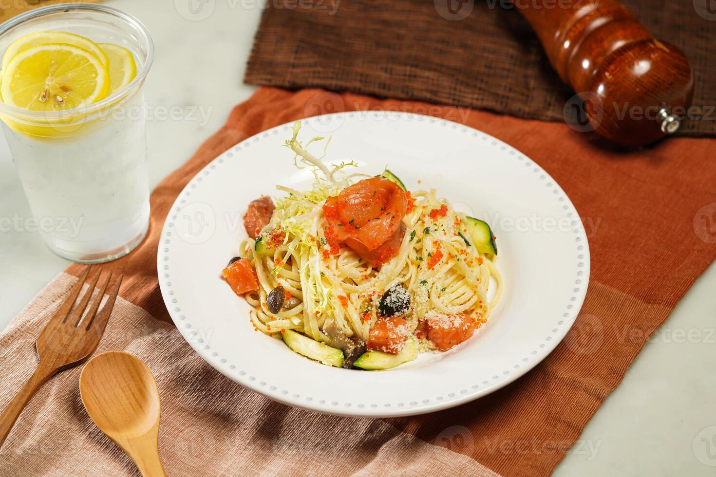 Linguine pasta with Crab Roe and Smoked Salmon in Japanese Style with lemonade, wooden spoon and fork served in plate isolated on napkin and dining table side view of italian food photo