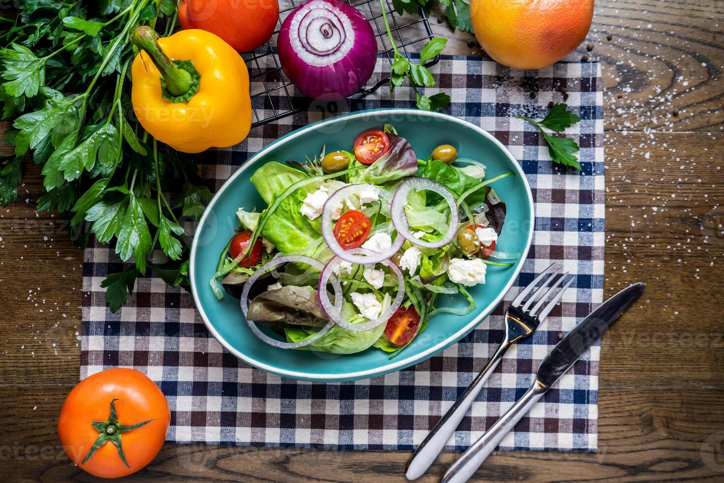 Toss The Green salad with spinach, cheese, olives, cherry tomato, tomato, onion, capsicum, coriander, knife and fork served in dish isolated on napkin top view of italian healthy food on wooden table photo