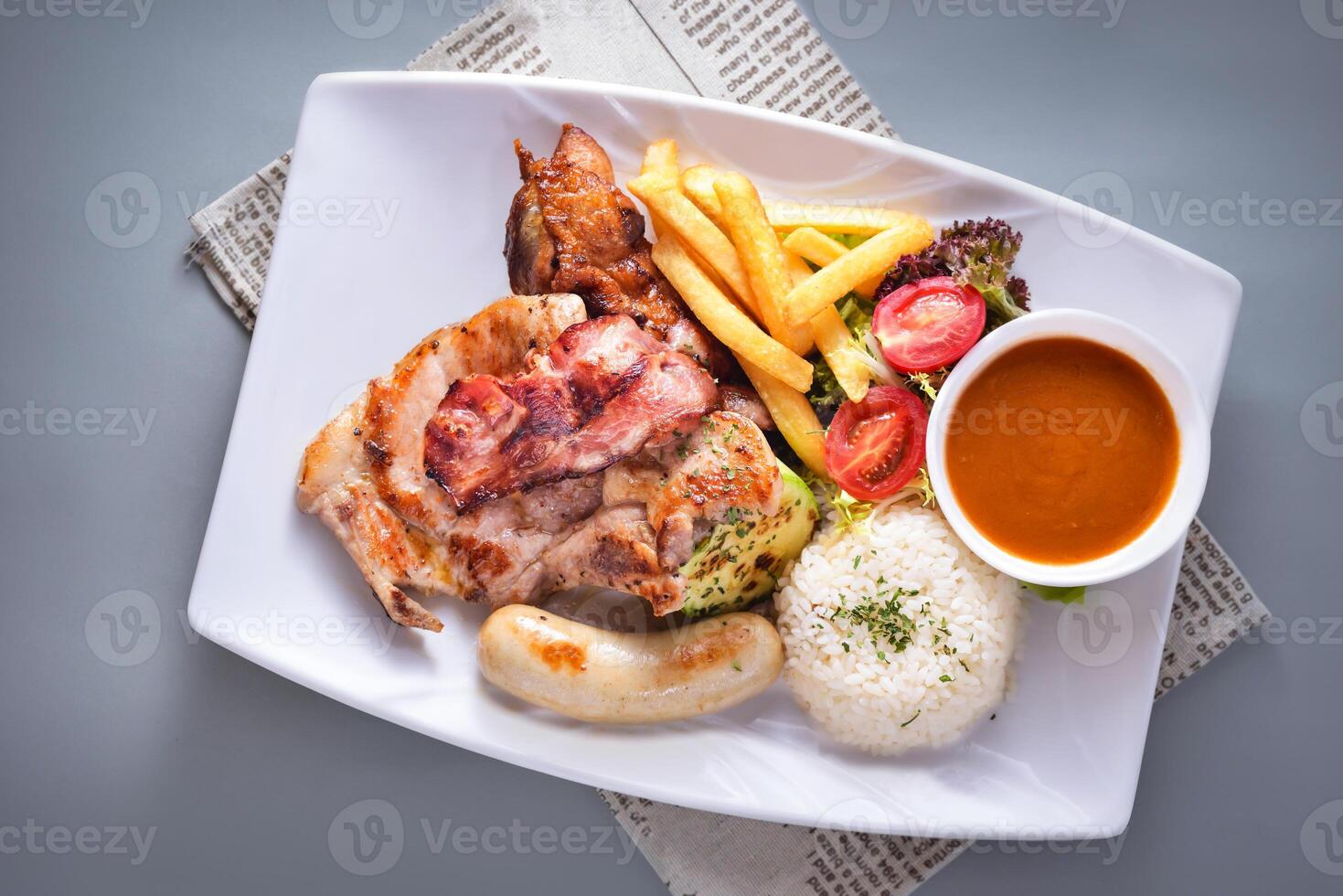 Miscellaneous steak platter with sausage, boiled rice, french fries, salad and sauce served in dish isolated on napkin top view of chinese food on grey background photo