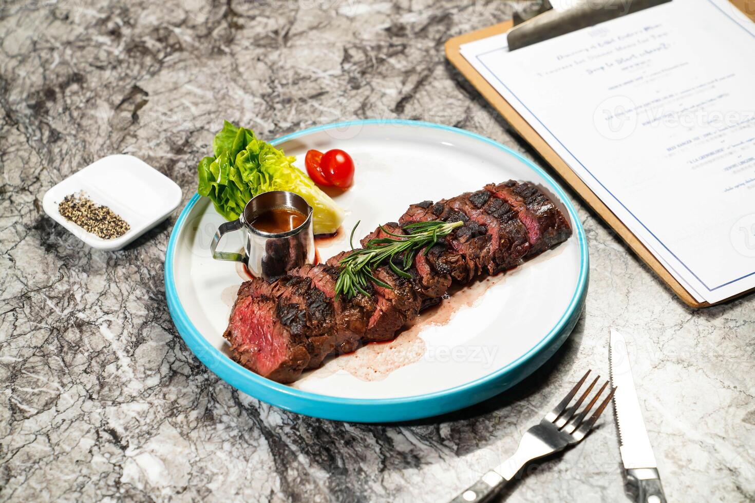 grilled Beef belly steak slice with butter, lettuce, cherry tomato, dip, fork and knife served in plate isolated on marble background side view of hong kong food photo