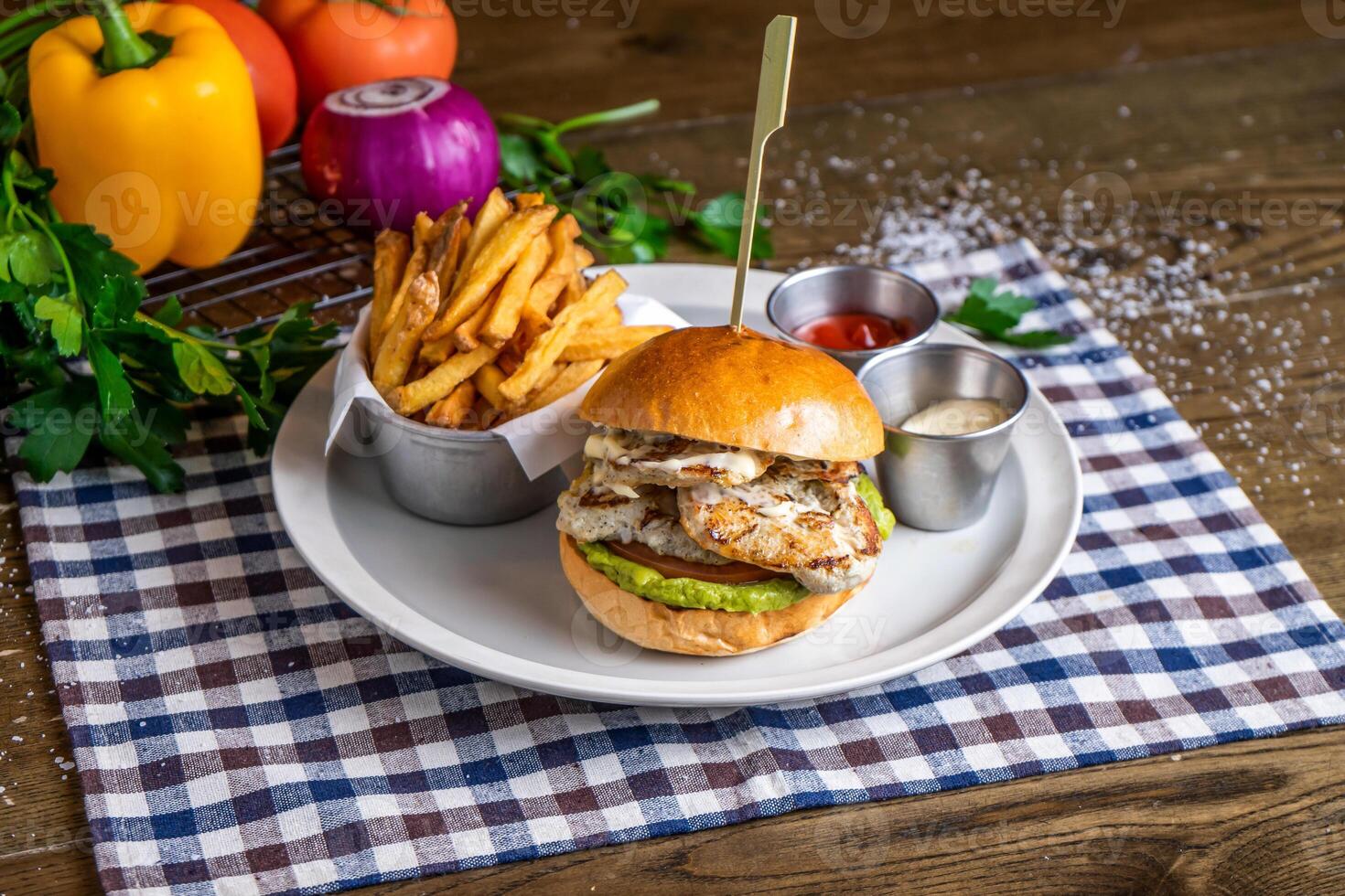 Chicken and Avocado Burger with french fries, ketchup, mayo dip, tomato, onion, capsicum, coriander, served in dish isolated on napkin side view of italian fastfood on wooden table photo