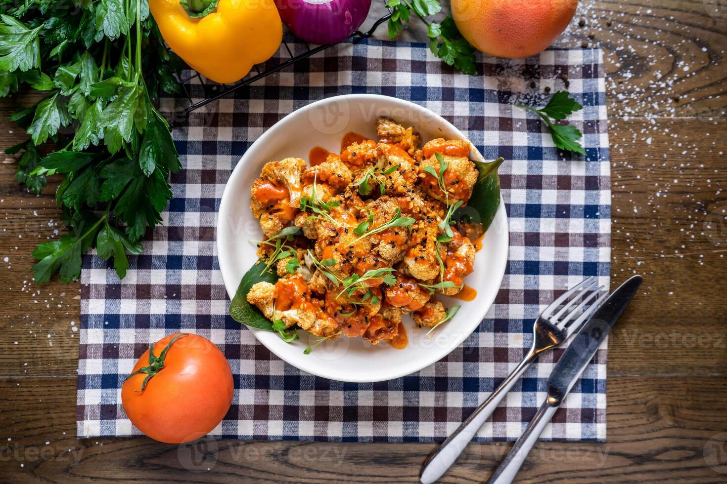 Cajun Cauliflower with sauce, tomato, onion, capsicum, coriander, knife and fork served in dish isolated on napkin top view of italian fastfood on wooden table photo