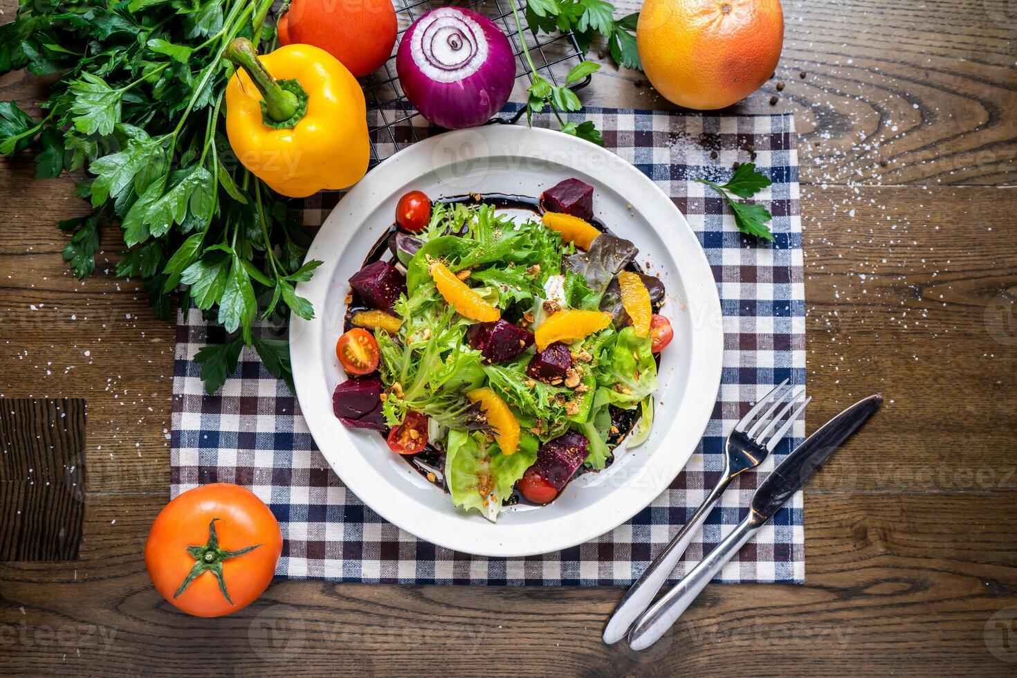 Roasted Beetroots Salad with orange, cherry tomato, spinach, tomato, onion, capsicum, coriander, knife and fork served in dish isolated on napkin top view of italian fastfood on wooden tablewith tomato, onion, capsicum, coriander, knife and fork served in photo