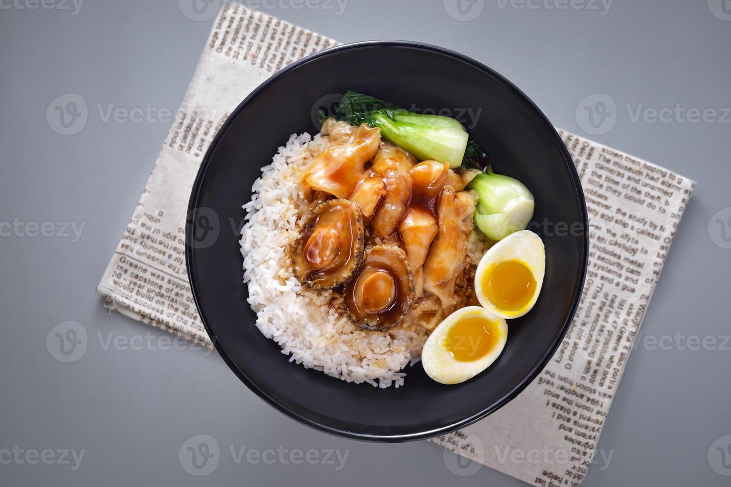 Abalone fish maw with rice with boiled egg and pickled vegetables served in bowl isolated on napkin top view of chinese food on grey background photo